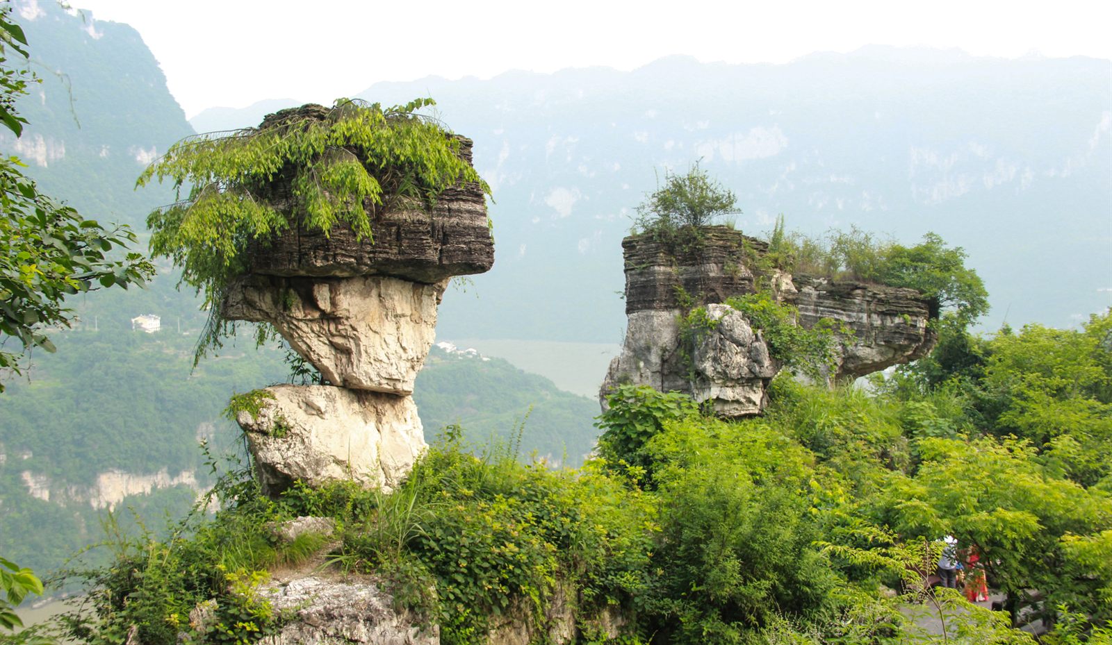 Tree-topped limestone rock pillars above a misty river valley in central China