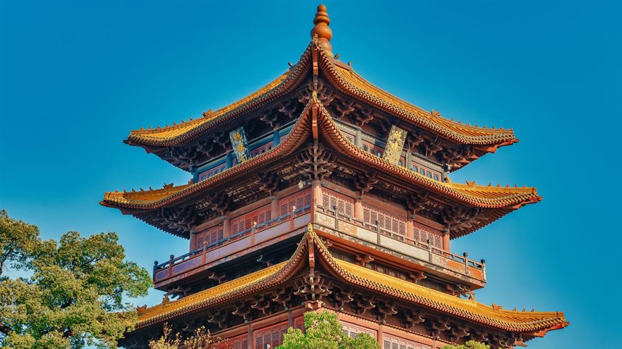 A multi-tiered traditional Chinese tower with red walls and golden eaves under a clear blue sky